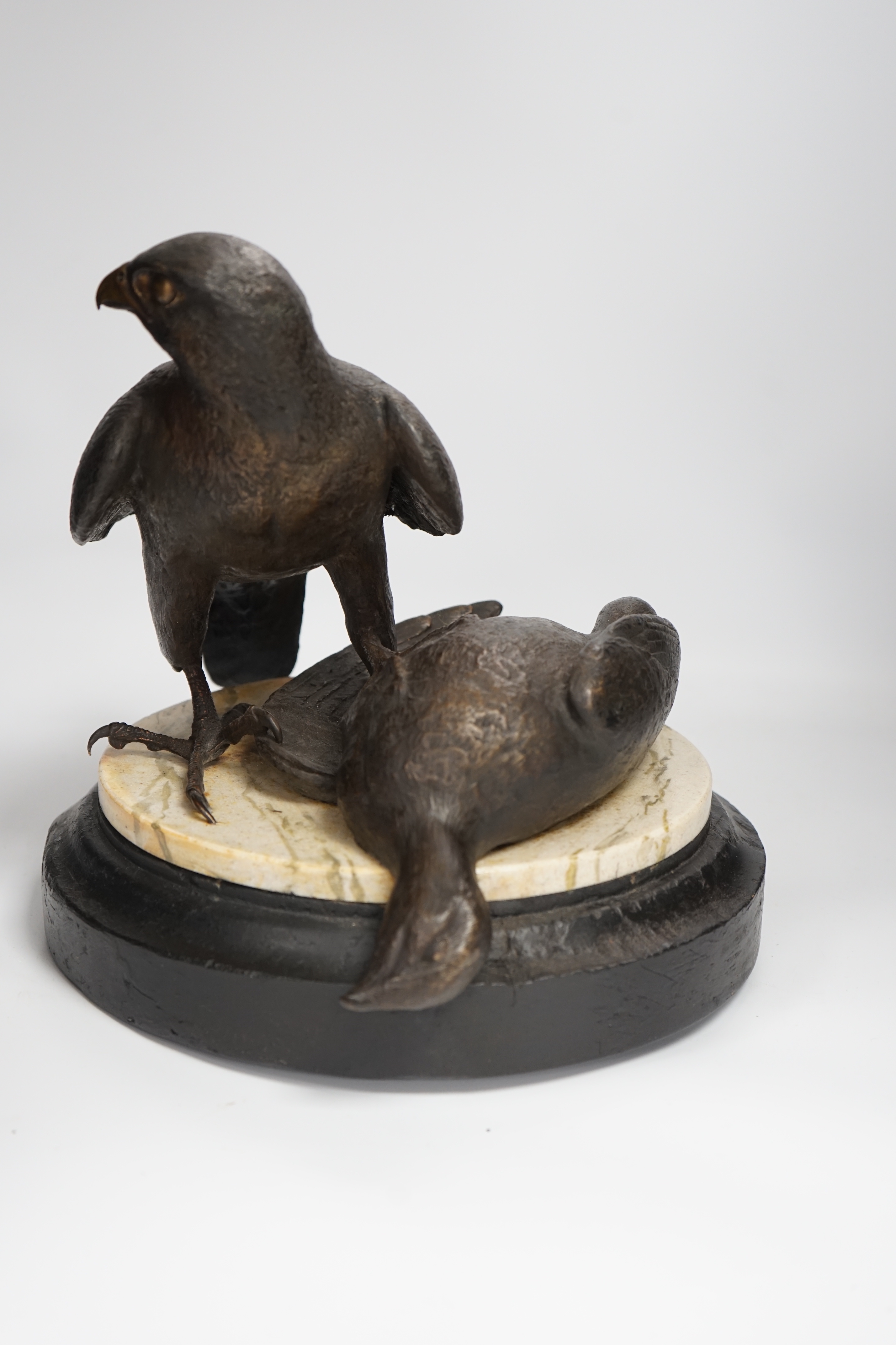 A limited edition bronze bird of prey with a kill, on a faux marble disc and painted wooden stand, 29cm high